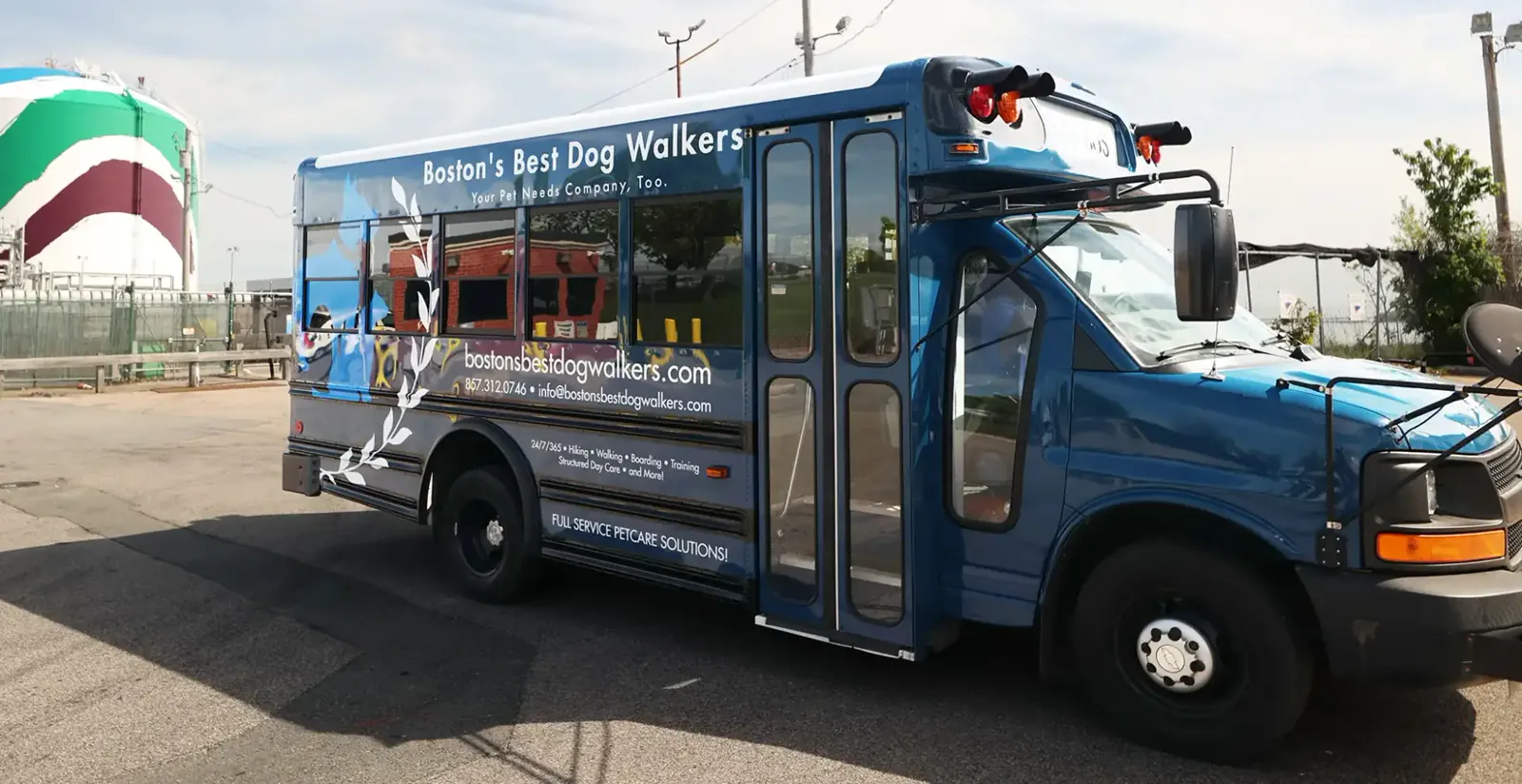 Boston’s Best Dog Walkers’ blue Bark Bus parked outdoors with company branding and pet care services displayed on the side.